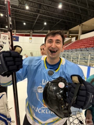 Matt in hockey gear on the ice, holding his helmet